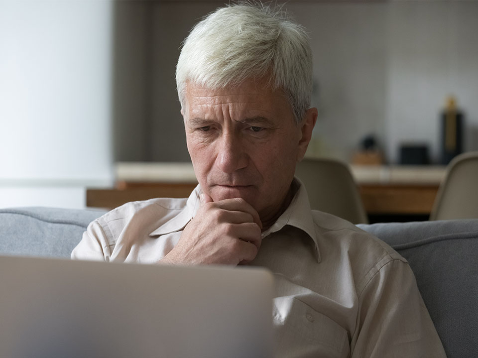 Mann sitzt lesend vor einem Laptop